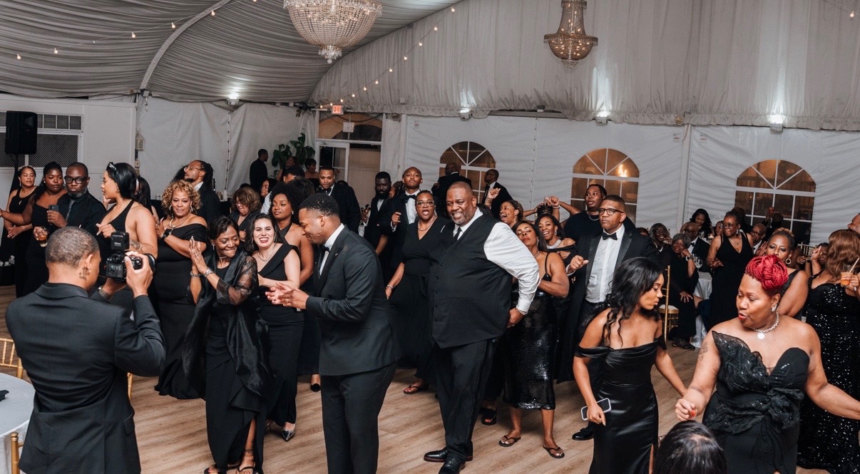 Full dance floor of wedding guests celebrating under chandeliers at a tented reception