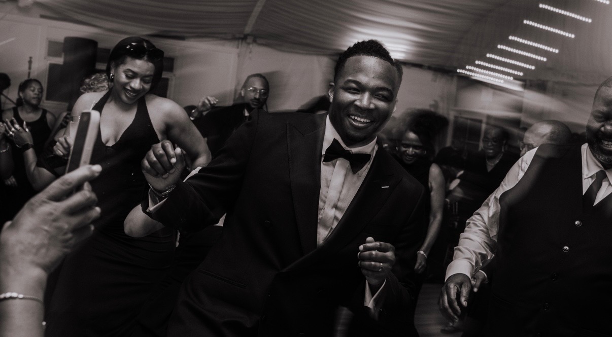 Black and white photo of a groom dancing with guests at a DMV wedding reception